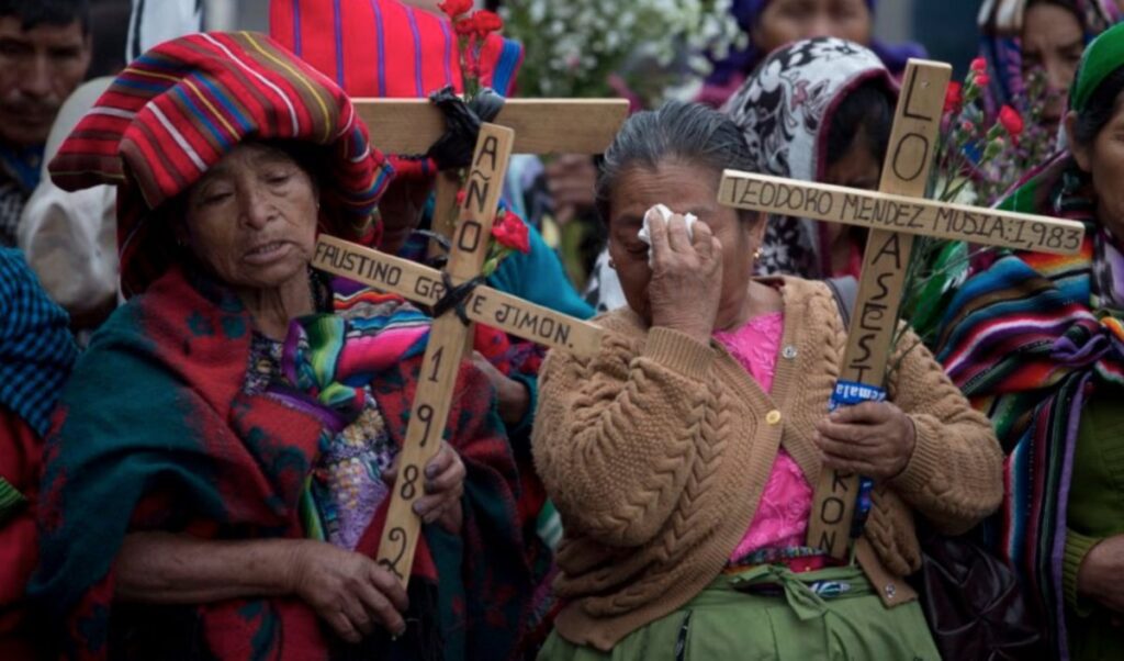 Two Guatemalan women holding wooden crosses with names of loved ones written on them