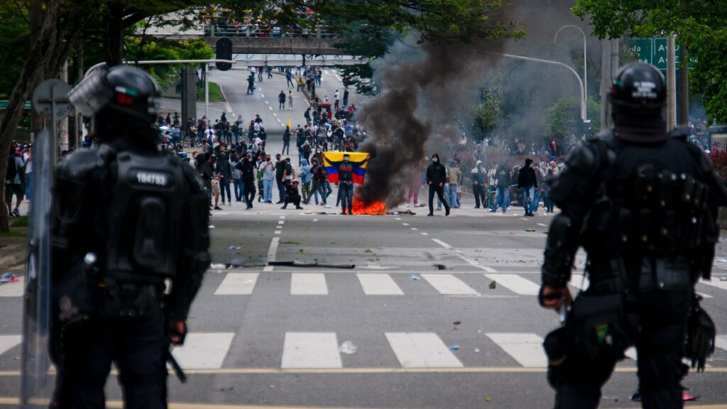Columbian protester carrying colombian flag standing in front of a fire on the street