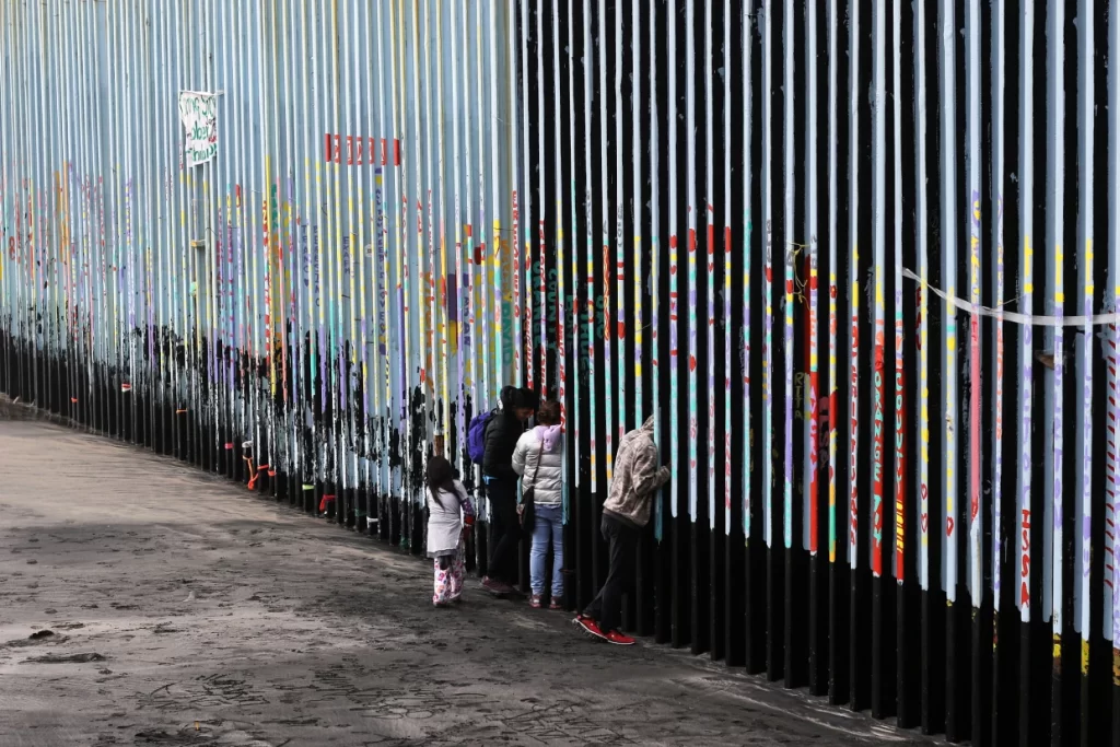A family of Central American migrants look through the U.S.-Mexico border fence, in Playas de Tijuana